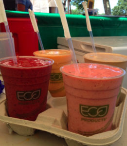 four delicious fruit smoothies with straws in biodegradable cups in a cardboard carrier